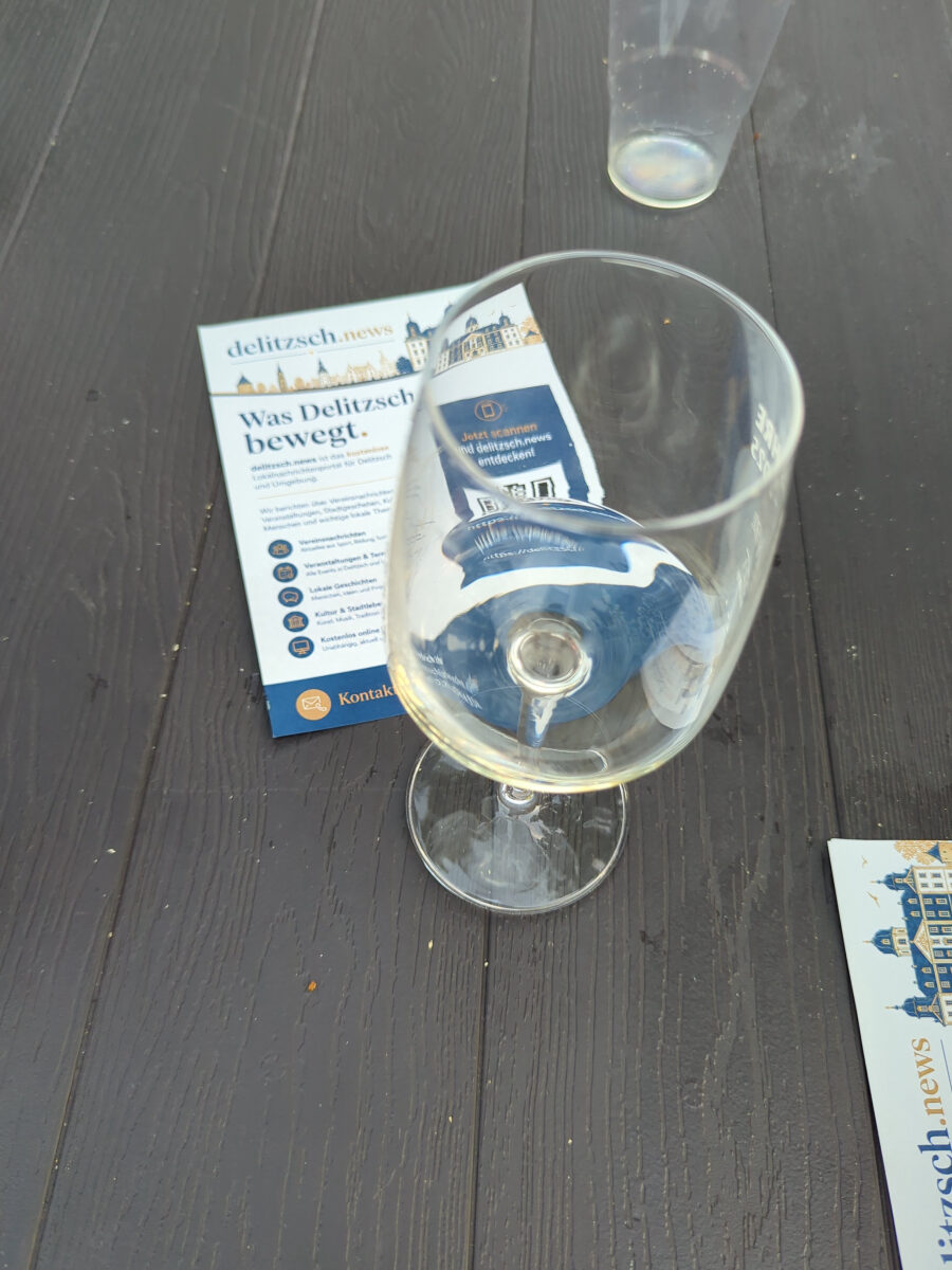 Glas und Flyer von delitzsch.news auf einem Tisch beim Abendmarkt