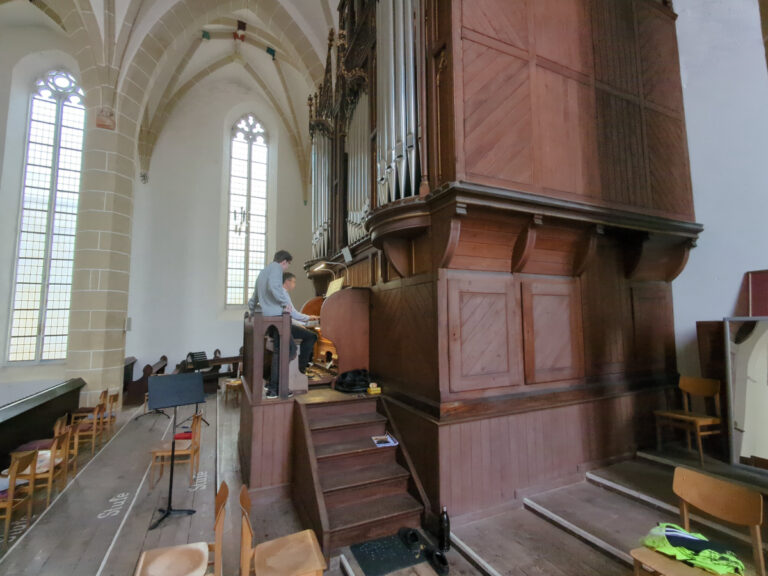 Jörg Topfstedt sitzt am Spieltisch der Rühlmann-Orgel; Niklas Müller steht neben ihm und unterstützt beim Ziehen der Register.