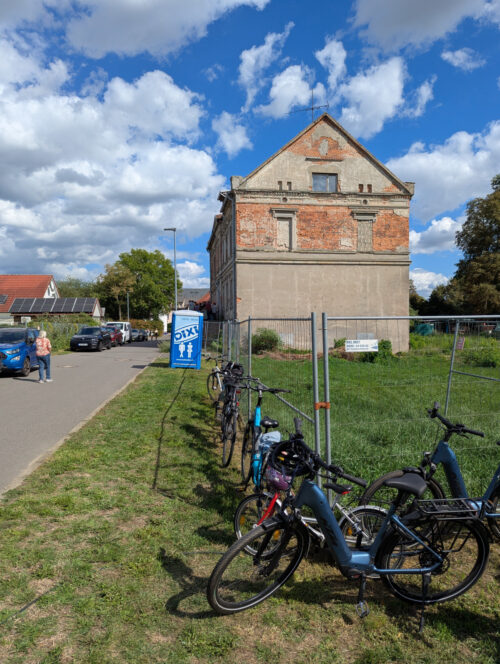 Fahrräder stehen am Bauzaun vor dem Herrenhaus in Storkwitz; an der Gebäudeseite hört eine Gruppe der Führung zu.