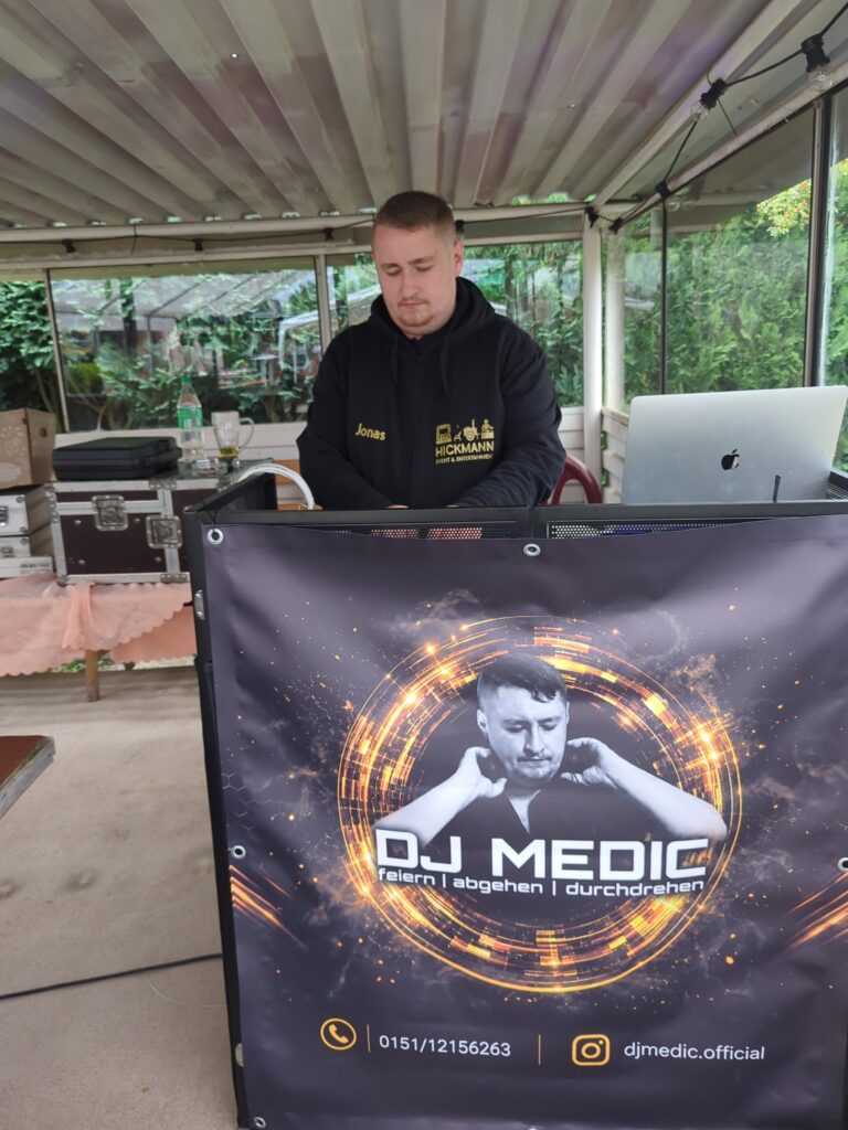 DJ Medic Jonas am Mischpult hinter seinem Veranstaltungsbanner beim KGV Gute Hoffnung