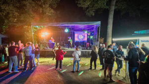 Gäste stehen am Abend vor der bunt beleuchteten Bühne beim Sommerfest im Döbernitzer Park.