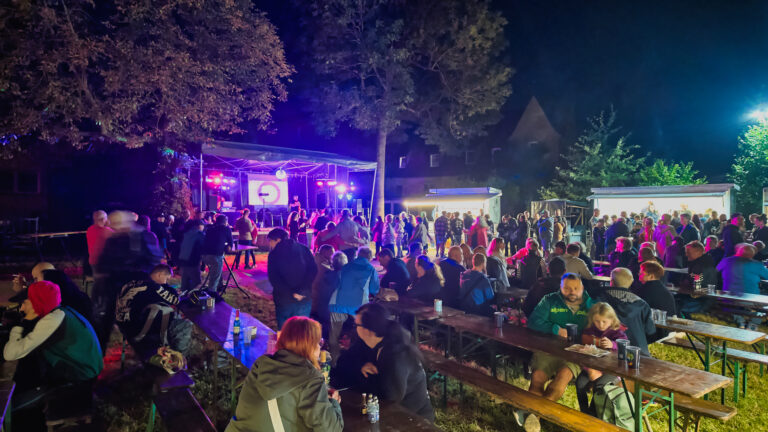Viele Gäste sitzen und stehen am Abend zwischen Bühne, Zelten und Bänken im Döbernitzer Park.