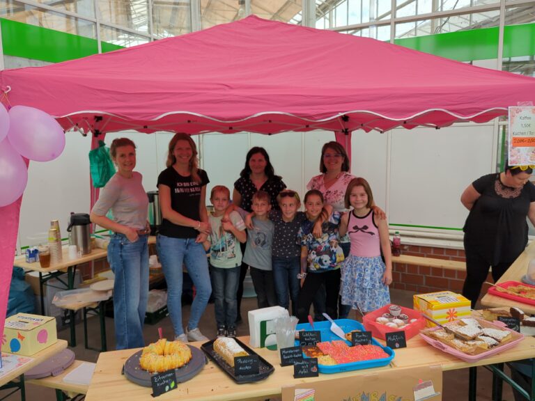 Kinder und Erwachsene stehen hinter dem Kuchenstand der Löwenklasse beim Hallenflohmarkt in Delitzsch.