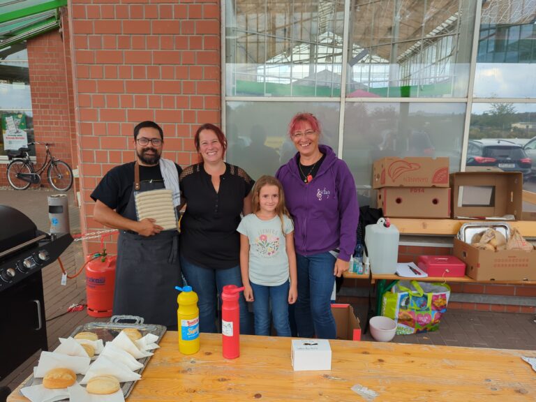 Das Team von SiTa’s steht mit einem Kind am Grillstand vor der Flohmarkthalle in Delitzsch.