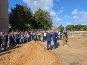 Gäste stehen beim Spatenstich für die neue Dreifeldsporthalle auf dem Baufeld der Artur-Becker-Oberschule.